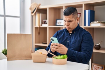 Fototapeta na wymiar Hispanic young man eating take away food using smartphone depressed and worry for distress, crying angry and afraid. sad expression.