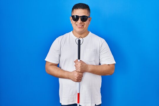 Hispanic young blind man holding cane smiling with a happy and cool smile on face. showing teeth.