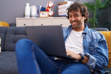 Young hispanic man using laptop sitting on sofa at home