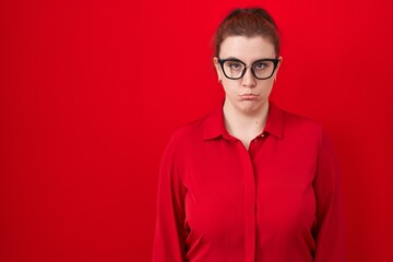 Young hispanic woman with red hair standing over red background depressed and worry for distress, crying angry and afraid. sad expression.