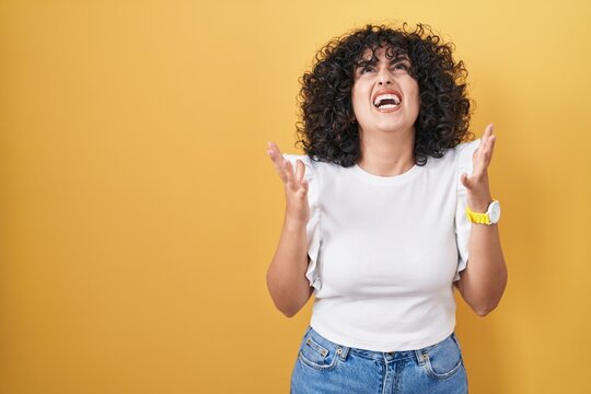 Young middle east woman standing over yellow background crazy and mad shouting and yelling with aggressive expression and arms raised. frustration concept.
