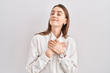 Young caucasian woman standing over isolated background smiling with hands on chest with closed eyes and grateful gesture on face. health concept.