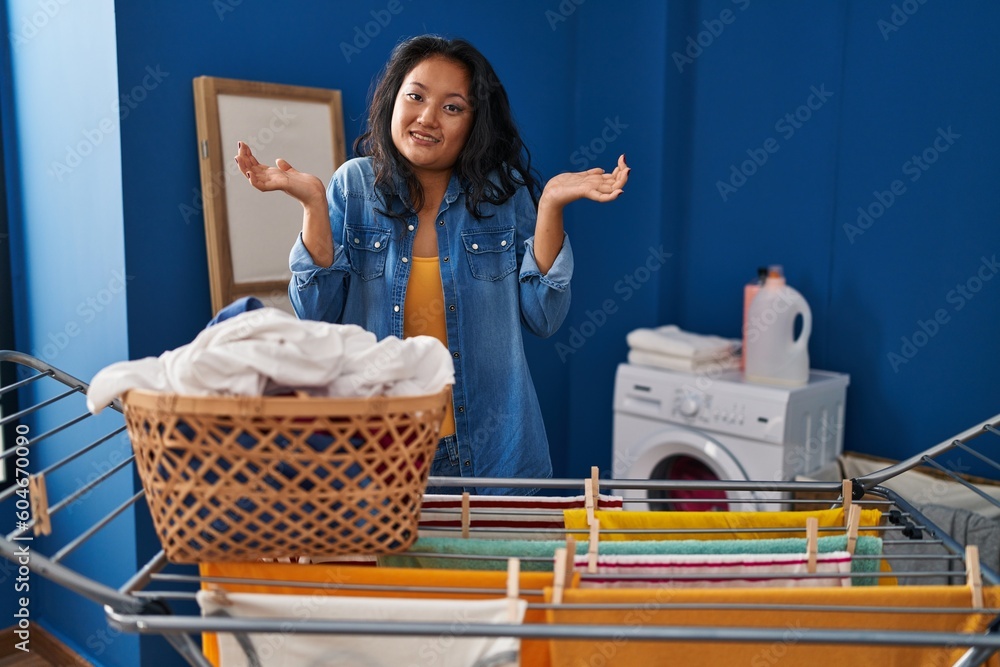 Sticker young asian woman hanging clothes at clothesline clueless and confused expression with arms and hand