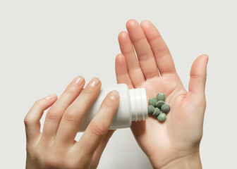 woman puts green herbal organic pills from a white jar in her palm. taking medicines, natural detox...
