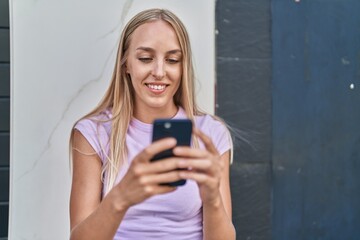 Fototapeta premium Young blonde woman smiling confident using smartphone at street