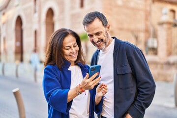 Middle age man and woman couple using smartphone standing together at street