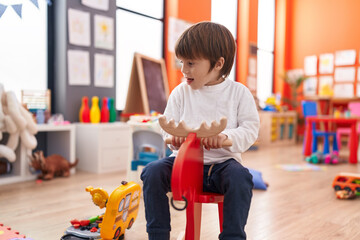 Obraz premium Adorable caucasian boy playing on reindeer rocking at kindergarten