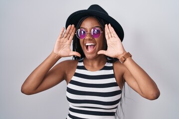 Young african american with braids wearing hat and sunglasses smiling cheerful playing peek a boo with hands showing face. surprised and exited