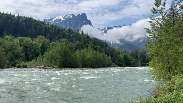 Flowing Skykomish river with snowcapped cascade mountains in Washington State during late spring season 
