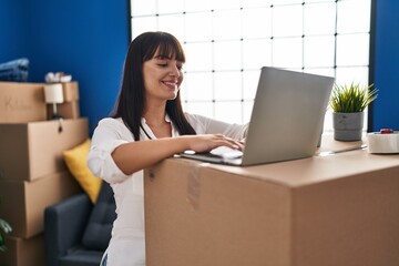 Young beautiful hispanic woman smiling confident using laptop at new home