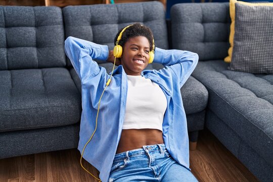 African american woman listening to music sitting on floor at home
