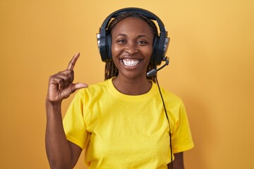 African american woman listening to music using headphones smiling and confident gesturing with hand doing small size sign with fingers looking and the camera. measure concept.