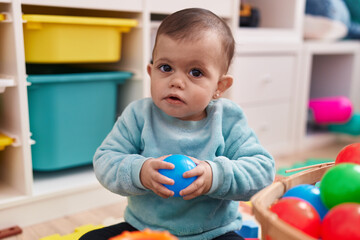 Adorable hispanic baby playing with balls sitting on floor at kindergarten