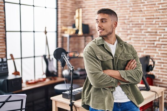 Young hispanic man musician standing with arms crossed gesture at music studio