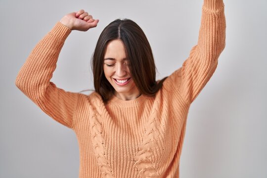 Young brunette woman standing over white background dancing happy and cheerful, smiling moving casual and confident listening to music