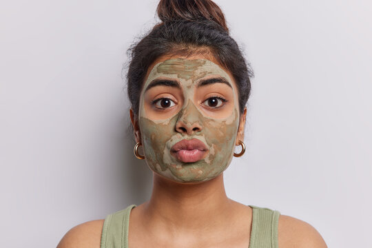 Portrait of pleasant looking young woman applies beauty mask to balance dry skin and minimise pores keeps lips folded stands bare shoulders isolated over white background. Facial treatments concept