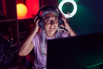 Middle age grey-haired woman streamer smiling confident sitting on table at gaming room