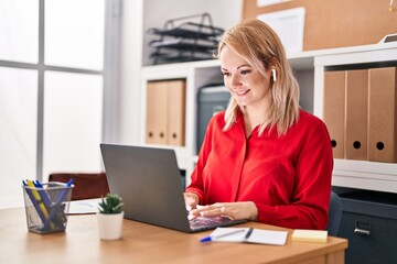 Young blonde woman business worker using laptop and earphones at office