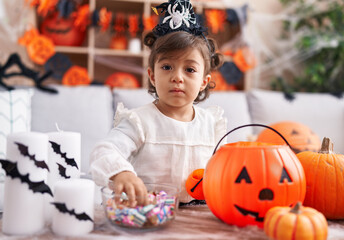 Fototapeta premium Adorable hispanic girl wearing halloween costume holding candies of bowl at home