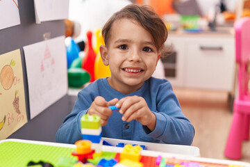 Adorable hispanic boy playing with construction blocks sitting on table at kindergarten