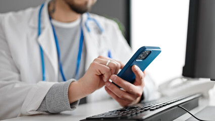 Fototapeta premium Hispanic man doctor using smartphone working at the clinic