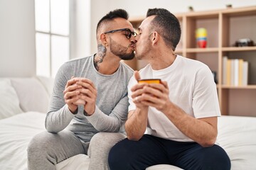Two men couple drinking cup of coffee kissing at bedroom