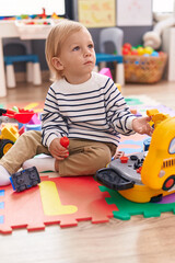 Adorable caucasian boy playing with tools toy sitting on floor at kindergarten