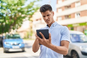Young hispanic man using touchpad with serious expression at street