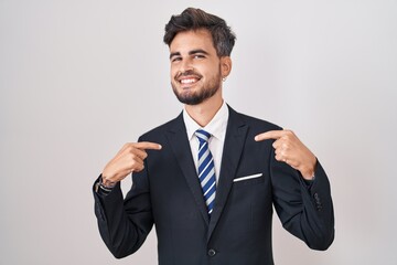 Young hispanic man with tattoos wearing business suit and tie looking confident with smile on face, pointing oneself with fingers proud and happy.