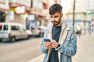 Young hispanic man using smartphone at street