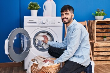 Young hispanic man smiling confident washing clothes at laundry room