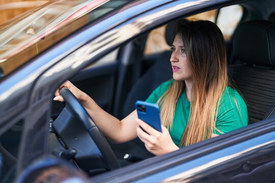 Young hispanic woman using smartphone sitting on car at street