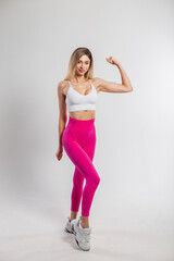 Fototapeta na wymiar Beautiful happy athletic fit girl with a slim body in fashionable sportswear with a top and pink leggings with sneakers poses and shows her biceps on a white background