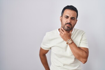 Hispanic man with beard standing over isolated background touching painful neck, sore throat for flu, clod and infection