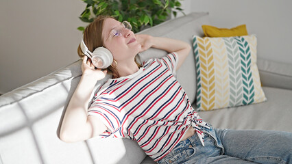 Young blonde woman listening to music sitting on sofa at home