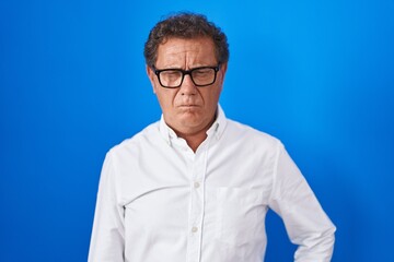 Middle age hispanic man standing over blue background skeptic and nervous, frowning upset because of problem. negative person.