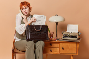 Busy displeased young redhead businesswoman prepares for formal meeting poses with paper documents...