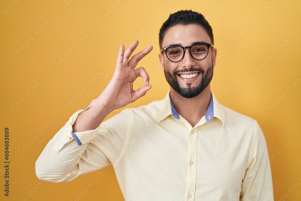 Wall mural Hispanic young man wearing business clothes and glasses smiling positive doing ok sign with hand and fingers. successful expression.