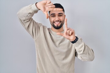 Young handsome man standing over isolated background smiling making frame with hands and fingers with happy face. creativity and photography concept.