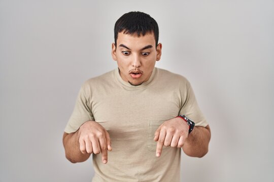 Young arab man wearing casual t shirt pointing down with fingers showing advertisement, surprised face and open mouth