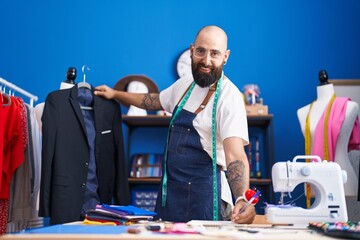 Young bald man tailor smiling confident holding jacket writing on notebook at clothing factory