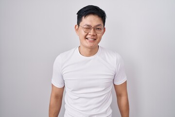 Fototapeta premium Young asian man standing over white background winking looking at the camera with sexy expression, cheerful and happy face.
