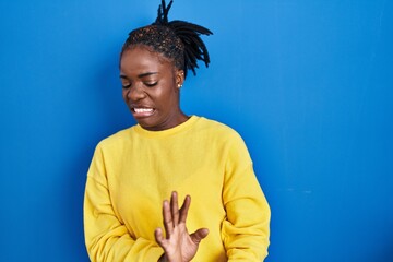 Beautiful black woman standing over blue background disgusted expression, displeased and fearful...