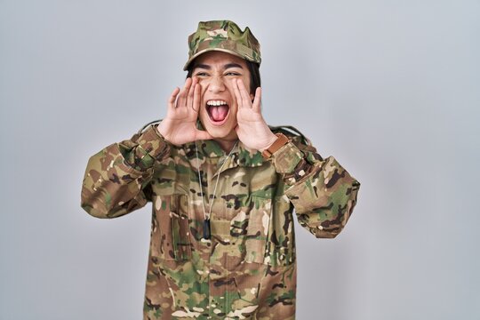 Young south asian woman wearing camouflage army uniform shouting angry out loud with hands over mouth