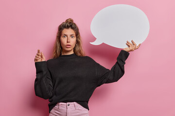 Studio shot of stunned beautiful woman holds white speech bubble stares impressed reacts to...