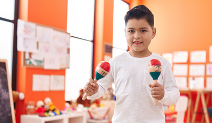 Adorable hispanic boy smiling confident playing maraca at kindergarten