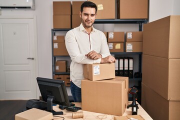 Young hispanic man e-commerce business worker leaning on packages at office