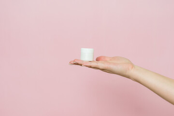 White jar or tube with cream (ointment) in hand. Facial care, bottle with cosmetic product without labeling.