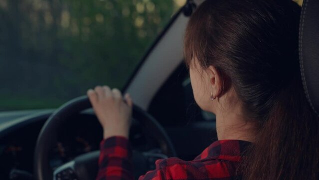 the woman driver behind the wheel dances and sings. happy fun trip. road highway track. an adult woman drives a car at sunset. car steering wheel concept. driving transport adventure vacation.