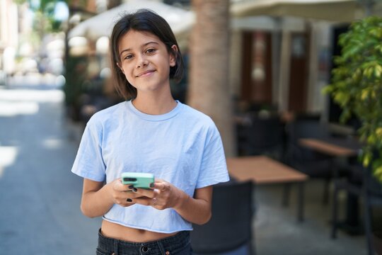Adorable hispanic girl smiling confident using smartphone at street